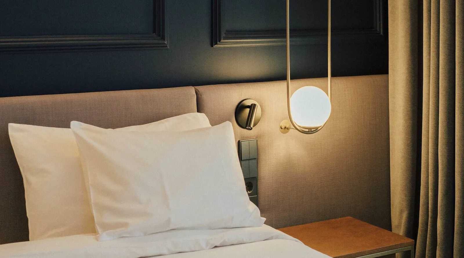 A bedroom with white linen and a brass reading light
