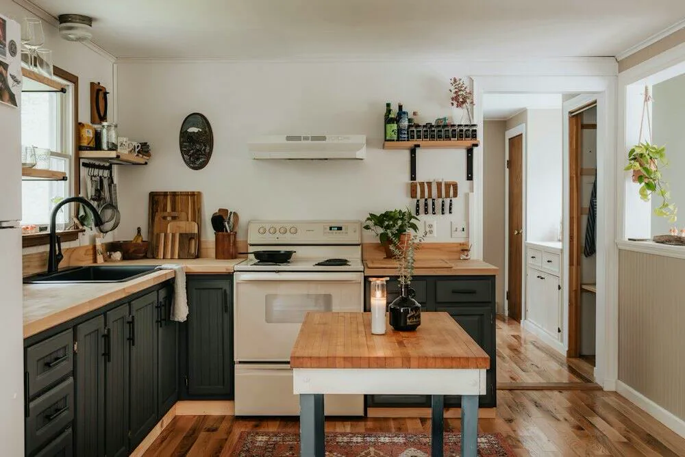 A small kitchen with dark green units and a wooden-topped island
