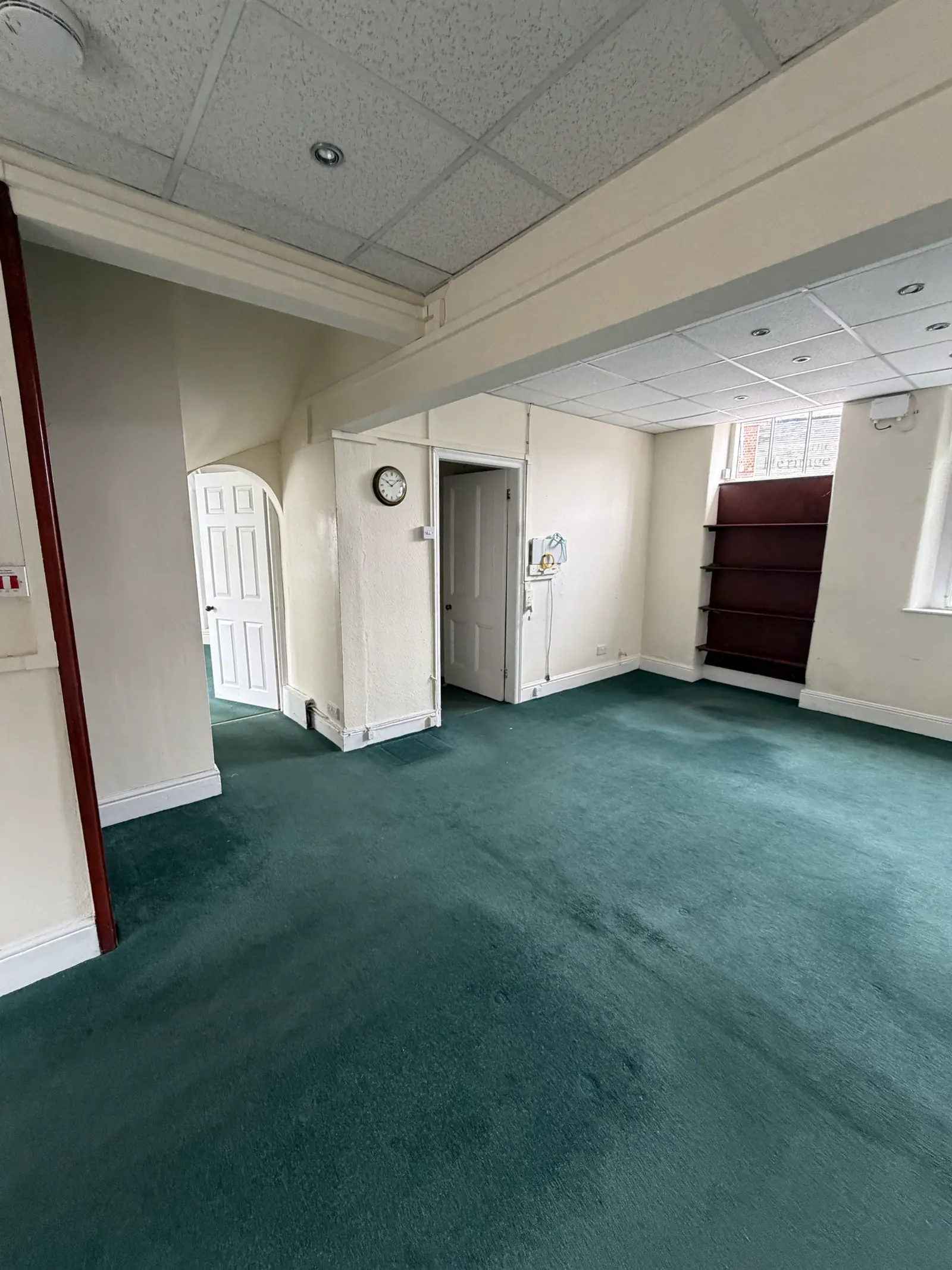 The ground-floor main office today: green carpet, ceiling tiles and an arched doorway