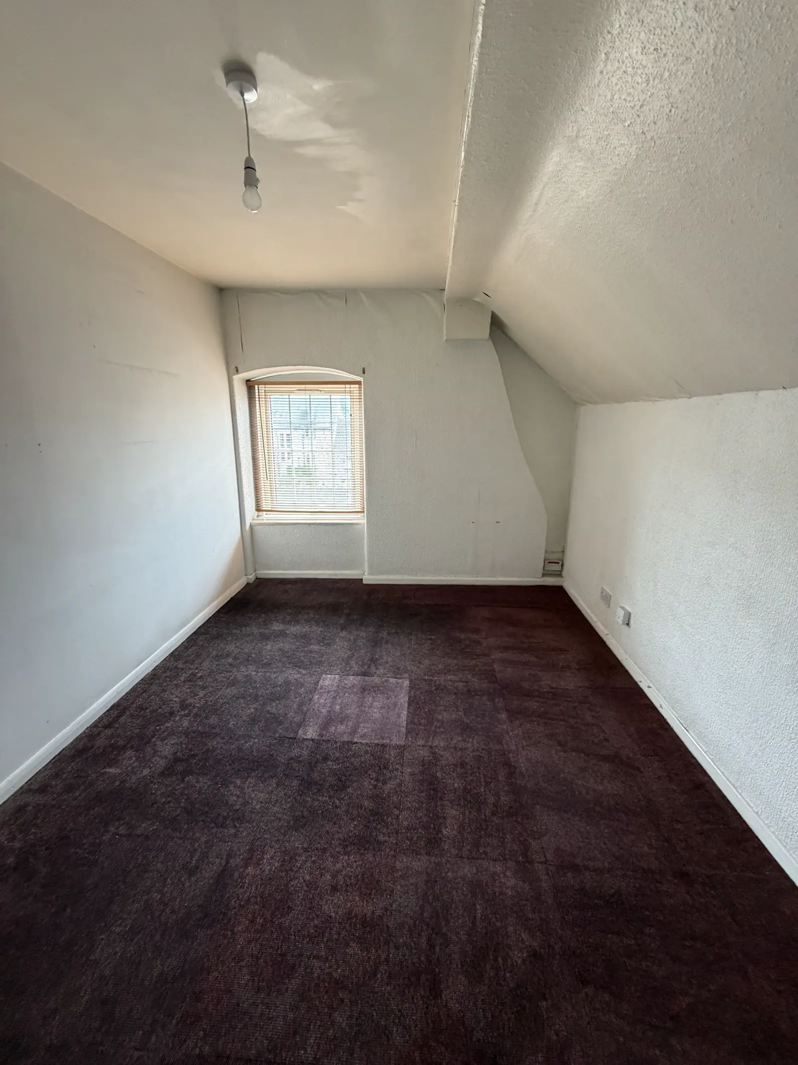 An empty second-floor room with a small window under the eaves